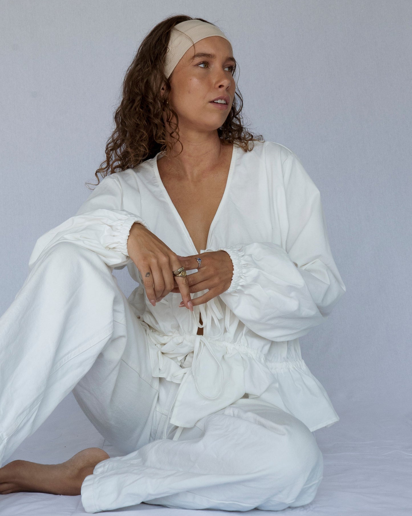 Woman wearing a white outfit sitting on a plain background