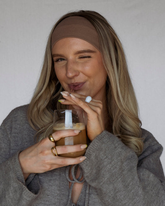 Woman drinking from a glass with a straw against a plain background
