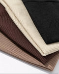 Stack of folded ribbed knit sweaters in black, beige, and brown on a white background